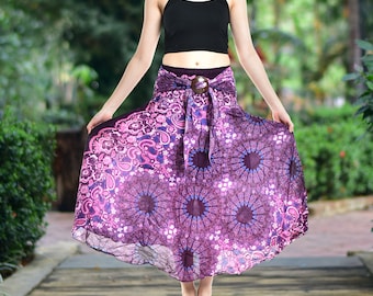 May include: A long, flowing skirt in shades of purple and magenta featuring a detailed mandala and paisley print. The skirt has an elasticized waistband with a decorative brown circular buckle at the center front and a tie-front fabric sash.