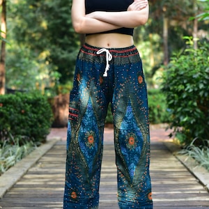 May include: Teal-colored patterned pants with an elastic waistband and drawstring. The pants feature an intricate design with orange and blue floral patterns. The person in the image is wearing a black tank top. The pants have pockets and are loose-fitting.
