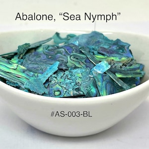 Pode incluir: Uma tigela branca cheia de fragmentos iridescentes de concha de abalone. As conchas exibem tons de azul, verde e roxo. O texto na parte superior diz "Abalone, 'Sea Nymph'" e na parte inferior "#AS-003-BL".