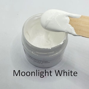 Könnte beinhalten: Ein kleines weißes Glas mit Pigmentpaste, beschriftet mit "Moonlight White". Ein Holzspatel entnimmt die weiße Paste.