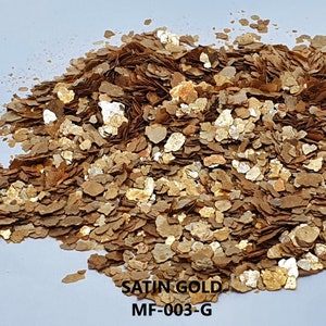 以下が含まれることがあります： 白い背景に「SATIN GOLD MF-003-G」という文字が書かれた、金と茶色の雲母フレークの山。雲母フレークは、キラキラ光る素材です。