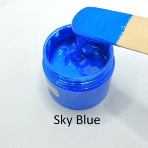 Peut inclure: Un petit pot de peinture bleu vif avec un bâtonnet en bois pour remuer la peinture. Le pot porte une étiquette indiquant "Sky Blue".