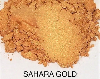 May include: A close-up of a pile of Sahara Gold mica powder. The powder is a warm, golden color with a slight shimmer.