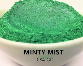May include: A close-up of a small bowl filled with a bright green, shimmery powder. The powder is labeled "Minty Mist #084-GR".