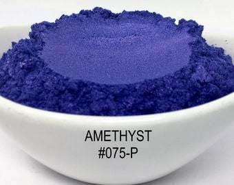 Puede incluir: Un pequeño cuenco blanco lleno de polvo de mica iridiscente de color morado oscuro. El polvo está etiquetado como "AMETHYST #075-P".