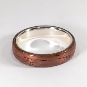 May include: A copper-coloured ring with a brushed finish and a silver band.
