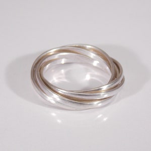 Pode incluir: Um anel de prata com cinco bandas entrelaçadas. O anel é liso e brilhante.