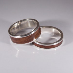 May include: Two silver rings with a brown wood inlay. The rings are stacked on top of each other.