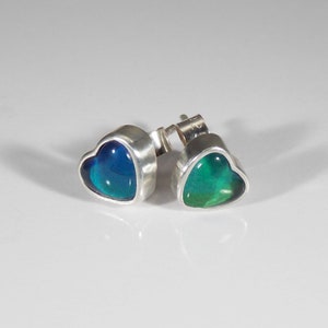 May include: A pair of silver heart-shaped earrings with iridescent blue and green gemstones.