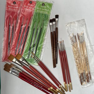Może przedstawiać: Asortyment pędzli artystycznych, w tym zestawy pakowane i pojedyncze pędzle. Zestawy pakowane są w czerwone i zielone plastikowe rękawy z napisem "PURE RED SABLE BRUSHES".