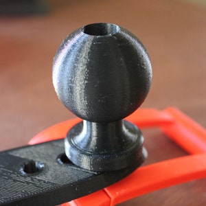 Op de afbeelding: Een zwarte 3D-geprinte kogelkop met een gladde, matte afwerking. De kogelkop is bevestigd aan een zwarte kunststof basis.