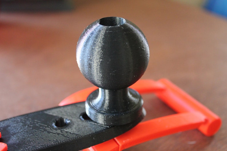 Op de afbeelding: Een zwarte 3D-geprinte kogelkop met een gladde, matte afwerking. De kogelkop is bevestigd aan een zwarte kunststof basis.
