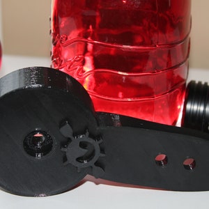 Op de afbeelding: Een zwart 3D-geprint onderdeel met een cirkelvormig ontwerp en drie gaten. Het onderdeel is gemaakt van plastic en heeft een gladde afwerking.