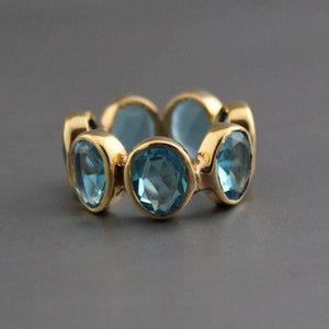 May include: A gold ring with a row of six oval-shaped blue gemstones.