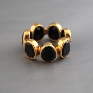 Puede incluir: Un anillo de oro con piedras preciosas negras engastadas en una banda circular.