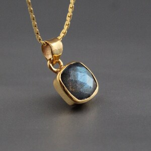 Puede incluir: Un collar de cadena de oro con un colgante cuadrado con una piedra de labradorita azul oscuro.