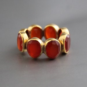 May include: A gold ring with six round, orange carnelian gemstones set in a continuous band.