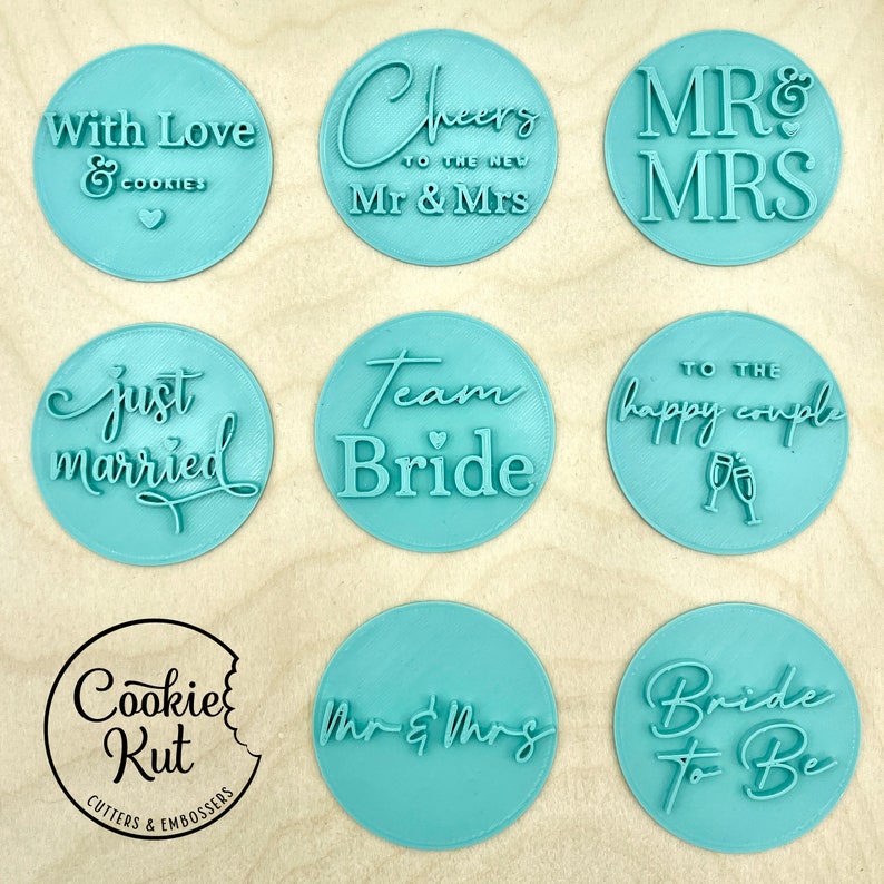 May include: Nine round cookie cutters with various wedding-themed phrases, including "With Love & Cookies", "Cheers to the New Mr & Mrs", "Mr & Mrs", "Just Married", "Team Bride", "To the Happy Couple", "Mr & Mrs", and "Bride to Be".