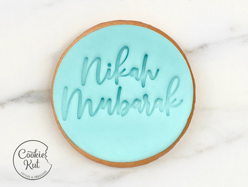 May include: A light blue round cookie with the words "Nikah Mubarak" written in white icing.
