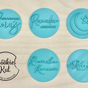 May include: A collection of light blue circular cookie cutters and embossers with Ramadan-themed designs. The cutters feature phrases like "Ramadan Mubarak" and "Keep us in your duas", along with a crescent moon and star. The Cookie Kut logo is also visible.
