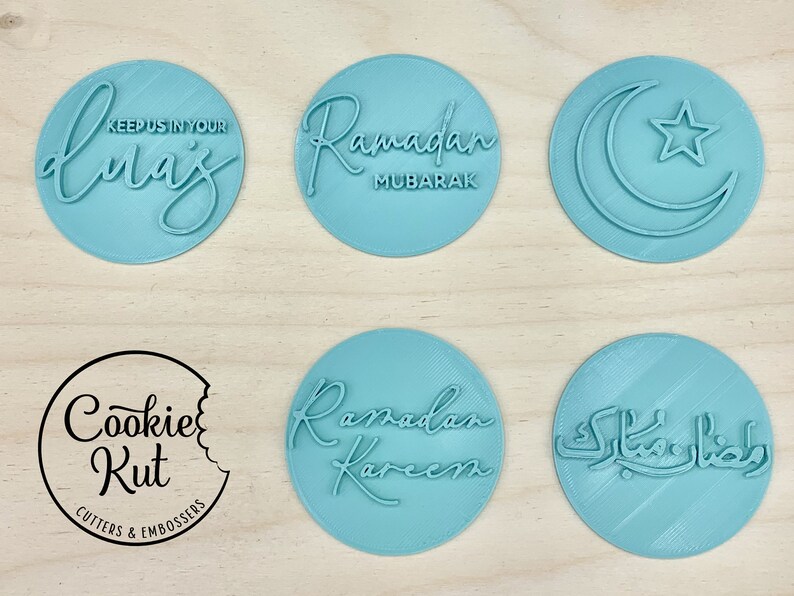 May include: A collection of light blue circular cookie cutters and embossers with Ramadan-themed designs. The cutters feature phrases like "Ramadan Mubarak" and "Keep us in your duas", along with a crescent moon and star. The Cookie Kut logo is also visible.