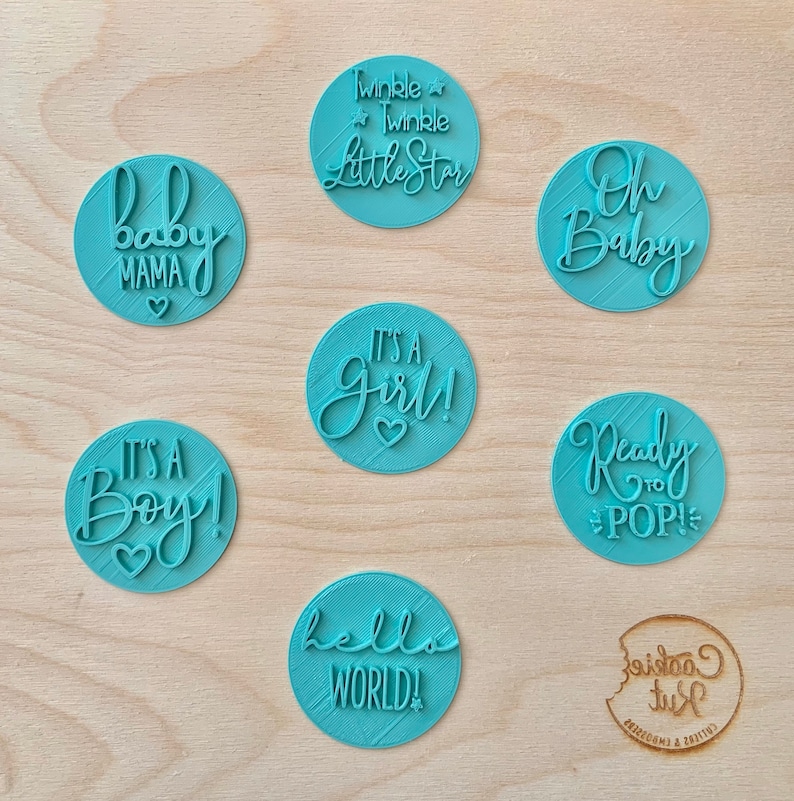 Op de afbeelding: Set van negen ronde blauwe koekjesuitstekers met verschillende babythema-zinnen, waaronder "Het is een jongen!" en "Twinkle Twinkle Little Star".