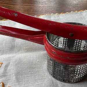 Metal 3.5”  potato ricer with red handle. Well preserved. works