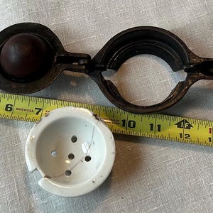 May include: A vintage metal citrus juicer with a round, brown, metal juicing cup and a metal handle. The juicer is on a white surface with a measuring tape.