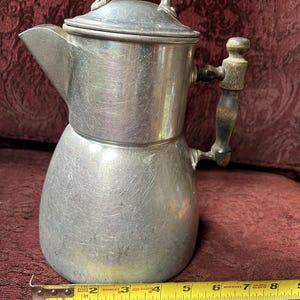 May include: A silver aluminum coffee pot with a wooden handle and lid. The pot is 7 inches tall.