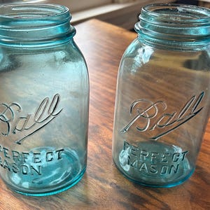 Op de afbeelding: Twee vintage blauwe glazen Ball Perfect Mason potten met het Ball logo en tekst.