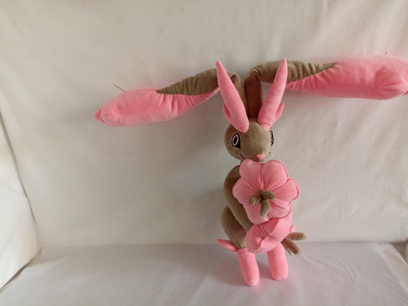 Puede incluir: Un conejo de peluche rosa y marr&oacute;n que sostiene una flor rosa. El conejo tiene orejas largas y un hocico largo.