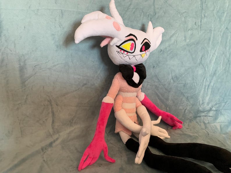 May include: A plush toy of a white and pink character with black horns, yellow eyes, and a pink and white striped dress. The toy has long pink arms and black legs.