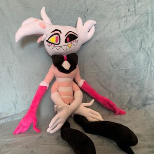 May include: A plush toy of a pink and white character with black eyes, a black bow tie, and pink and black striped arms and legs.