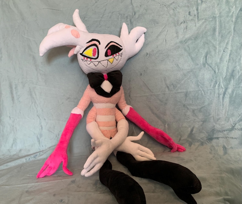 May include: A plush toy of a pink and white character with black eyes, a black bow tie, and pink and black striped arms and legs.