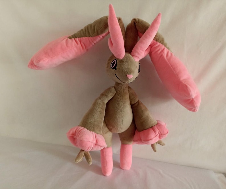 Puede incluir: Un juguete de peluche de conejo con pelaje marr&oacute;n y orejas y patas rosas. El conejo tiene una nariz larga y puntiaguda y ojos grandes y negros.