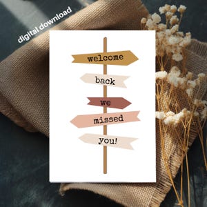 Puede incluir: Tarjeta de descarga digital con un diseño de señal de tráfico. La señal tiene flechas en tonos marrones y rosas, cada una con una palabra: "welcome", "back", "we", "missed" y "you!". Las palabras están en una fuente sencilla. La tarjeta está sobre una superficie de arpillera.
