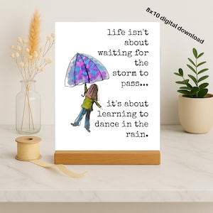 Könnte beinhalten: Digitaldruck auf einem Holzständer. Der Druck zeigt eine Aquarellillustration einer Person, die einen Regenschirm im Regen hält, mit dem Text "life isn't about waiting for the storm to pass... it's about learning to dance in the rain."