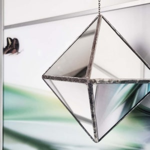 Puede incluir: Un adorno colgante geométrico de forma de diamante plateado con paneles de vidrio espejados.