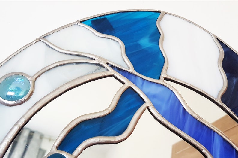 Op de afbeelding: Close-up van een glas-in-loodspiegel met een blauw en wit ontwerp. De spiegel is ingelijst met zilverkleurig metaal.