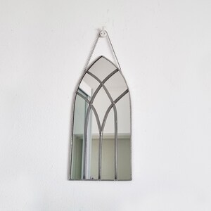 May include: A silver-framed arched mirror with a stained glass design. The mirror is hanging on a white wall.