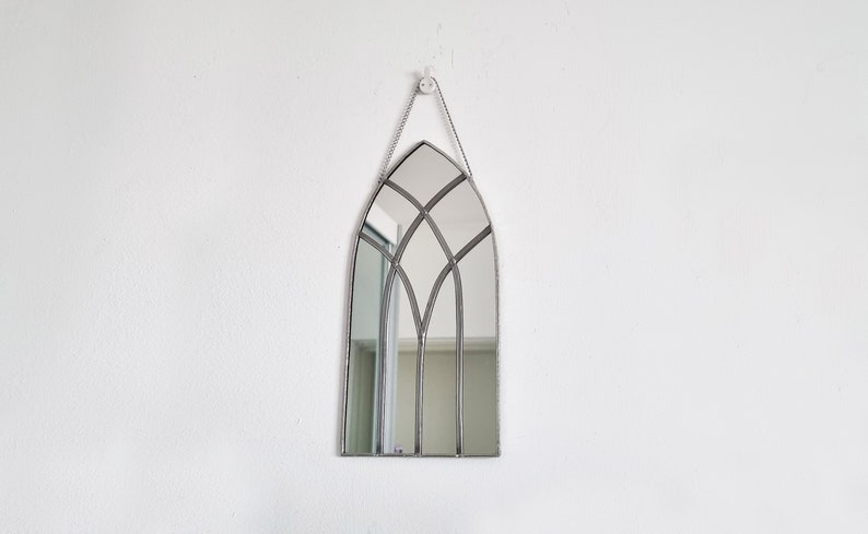 May include: A silver-framed arched mirror with a stained glass design. The mirror is hanging on a white wall.