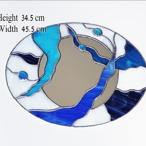 Op de afbeelding: Ovale spiegel van gekleurd glas met een abstract ontwerp in blauw, wit en zwart. De spiegel is 34,5 cm hoog en 45,5 cm breed.
