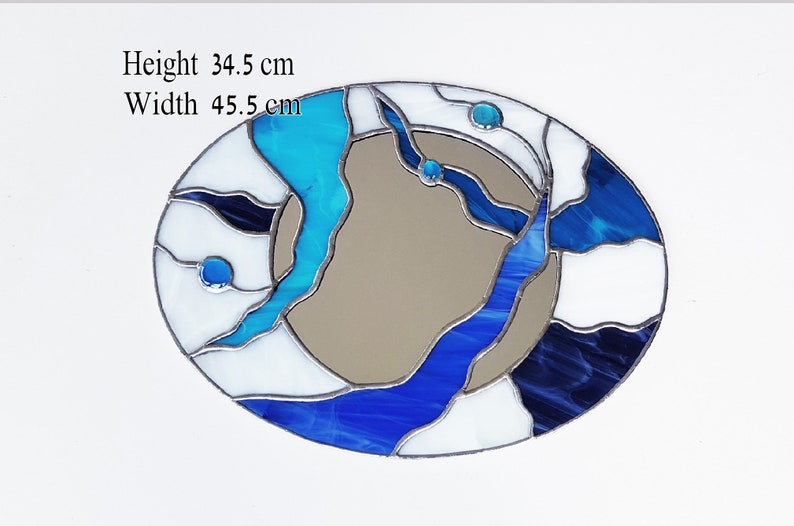 Op de afbeelding: Ovale spiegel van gekleurd glas met een abstract ontwerp in blauw, wit en zwart. De spiegel is 34,5 cm hoog en 45,5 cm breed.