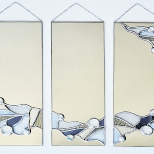 May include: Three rectangular mirrors with a stained glass design featuring abstract shapes in shades of blue, white, and beige. The mirrors are hung on a white wall.