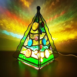 May include: A stained glass Christmas tree lamp with a green base and colorful ornaments. The lamp is lit and casting a warm glow.