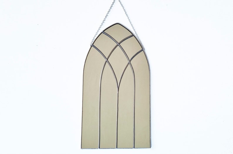 May include: A silver arched mirror with a stained glass design. The mirror is hanging from a silver chain.
