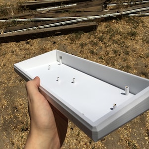 Puede incluir: Caja de teclado de plástico blanco con cinco pequeños agujeros para tornillos.