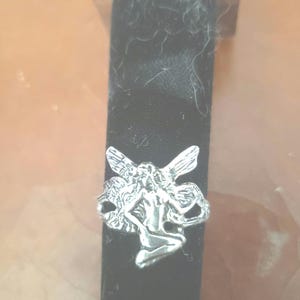 May include: A silver ring with a detailed fairy design. The fairy is sitting with wings spread out.