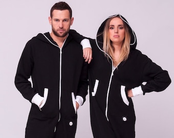 May include: Two people wearing black hooded one-piece pajamas with white trim. The pajamas have a zipper down the front and pockets on the sides.