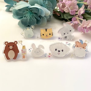 May include: A set of eight clear acrylic pins featuring various animal designs. The pins include a brown bear, a white rabbit, a white dog, a hamster, a frog, a tiger, and a grey puppy. The pins are decorated with small hearts, stars, and flowers.